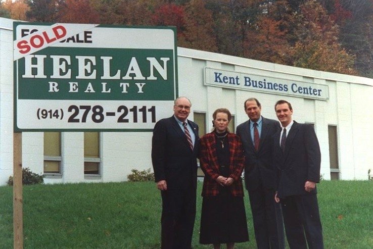 Ed Heelan, left, and Doug Heelan, right, with clients beside a Heelan Realty Sold sign, circa 1993.
