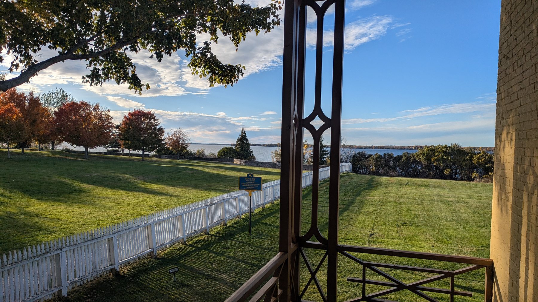 View from a porch across a lawn and white fence toward the water at Sackets Harbor.